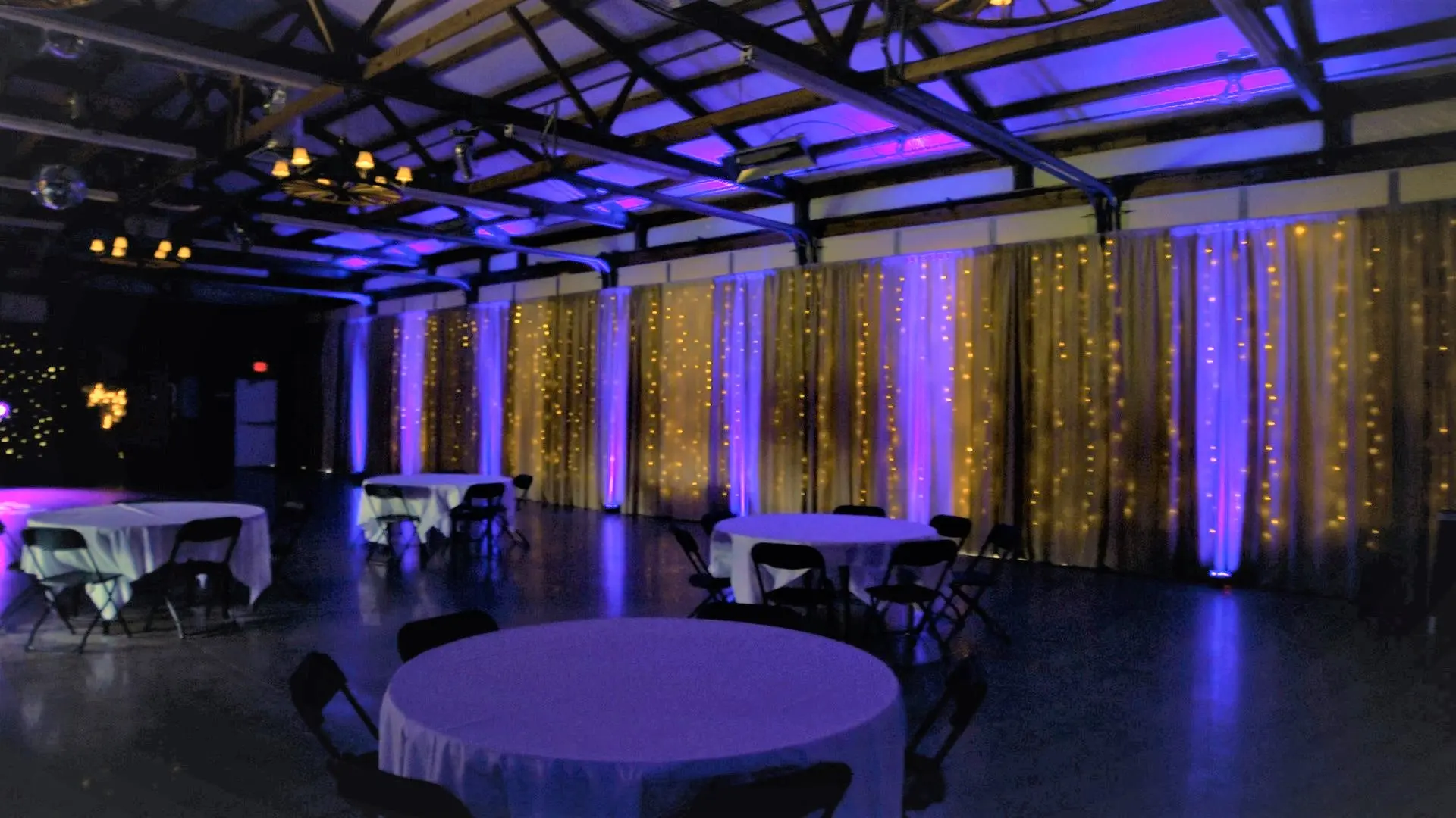 Wedding reception room transformed with deluxe uplighting and warm curtain lights